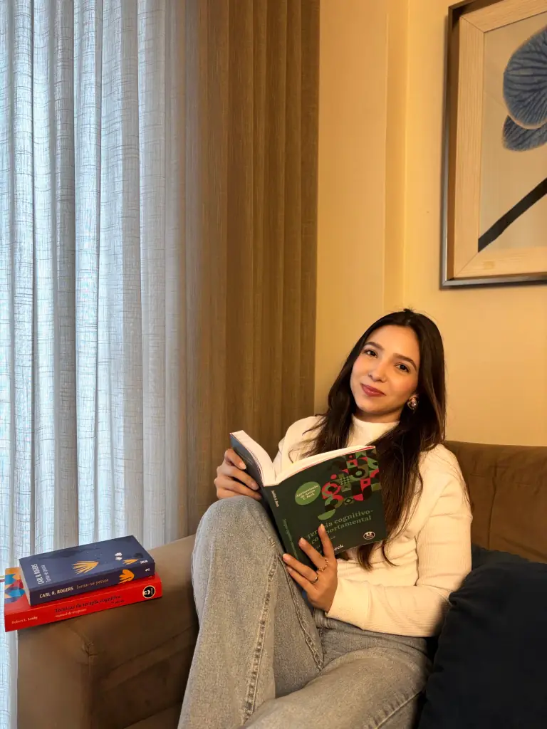 Bruna Boave sentada em um sofá, lendo um livro de terapia cognitivo-comportamental